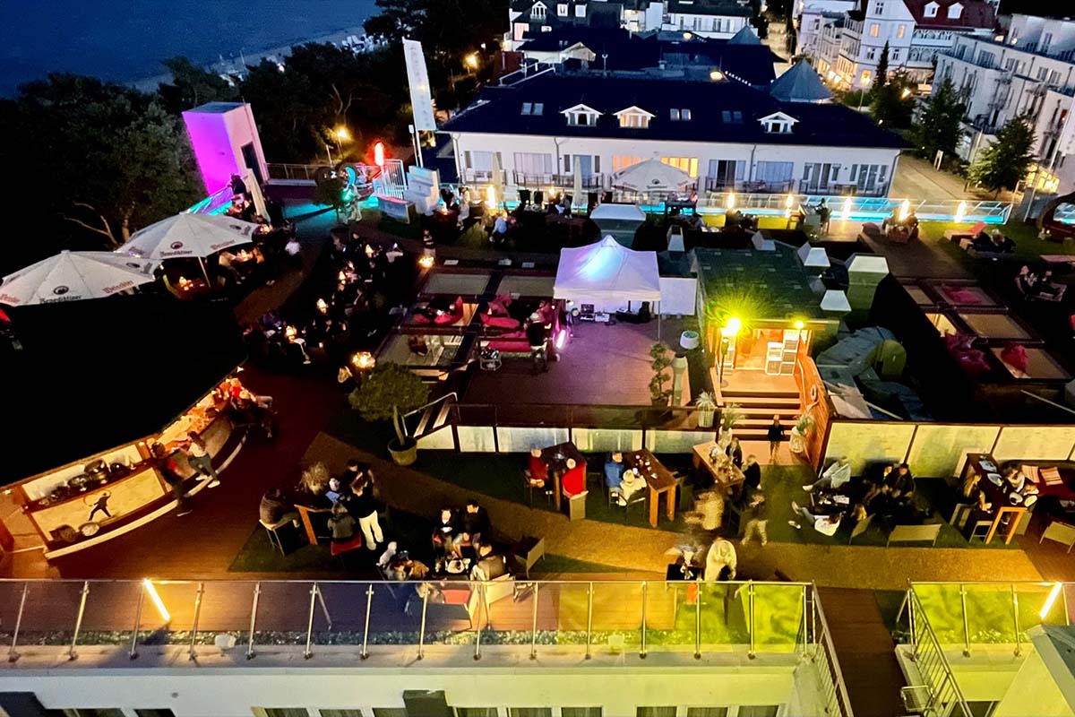 Stimmungsvoll beleuchtete Dachterrasse mit Sommergästen in der Arkona Sky Bar des Arkona Strandhotels auf Rügen.