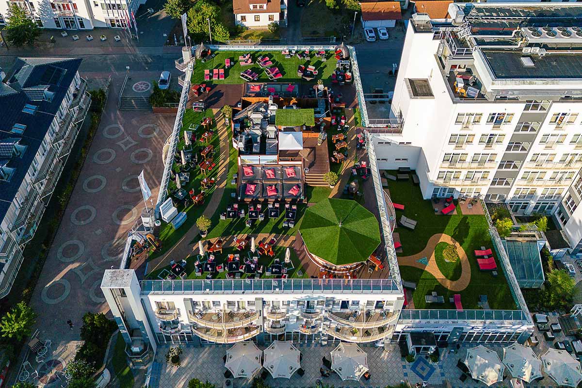 Luftaufnahme des Arkona Strandhotels auf Rügen mit Arkona Sky Bar Dachterrasse voller Sommergäste.