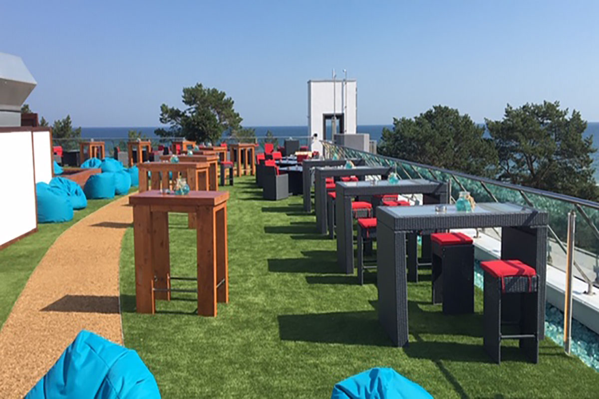 Die begrünte Dachterrasse der Arkona Sky Bar mit Sitzmöglichkeiten, blauen Sitzsäcken und einem Blick auf die Ostsee.