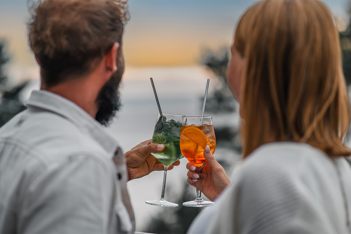 Zwei Cocktails im Vordergrund beim Anstoßen eines Paares in der Arkona Sky Bar mit Blick auf die Ostsee